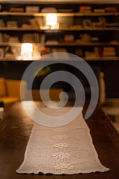 Vertical shot of a wooden table with white tablecloth against a blurred background of bookstand