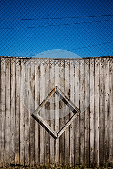 Vertical shot of a wooden wall and a chain link fence under the blue sky