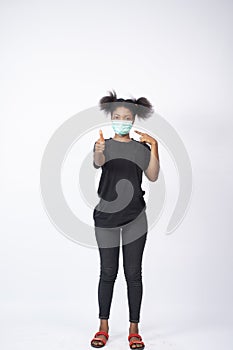 Vertical shot of a young African lady wearing a face mask, giving thumbs up and pointing to the mask