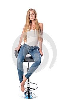 Vertical shot of a young beautiful long haired woman seating on an office or bar chair isolated on white background.