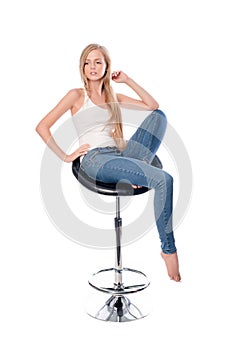 Vertical shot of a young beautiful long haired woman seating on an office or bar chair isolated on white background.