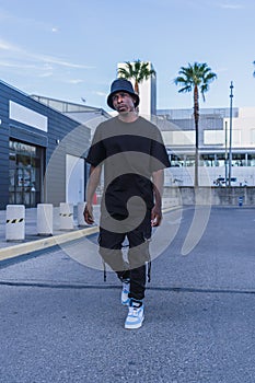 Vertical shot of a young black man in street-style clothes confidently walking outdoors