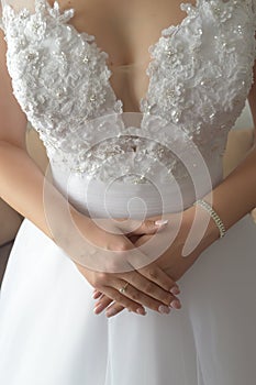 Vertical shot of young Caucasian bride in lacy revealing wedding dress, holding her hands crossed and showing proudly her ring