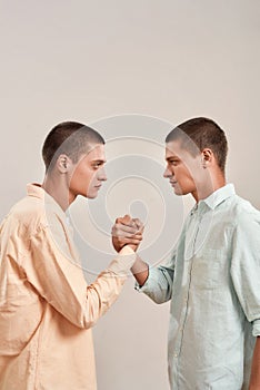 Vertical shot of young caucasian twin brothers looking at each other, holding hands while standing face to face isolated
