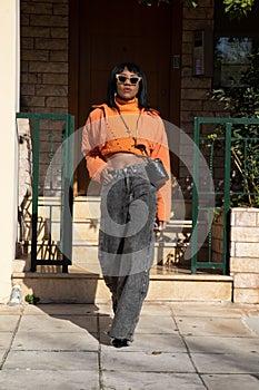 Vertical shot of a young fashionable African American woman in an orange jacket and gray baggy jeans