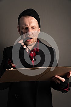 Vertical shot of a young man who holds a felttip pen in his mouth to write text on cardboard. begging concept photo