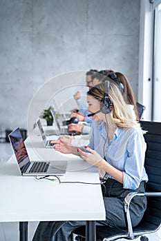 Vertical side view of beautiful blond hair call canter agent working with group of operators in office.