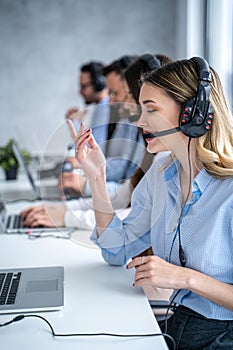 Vertical side view of beautiful blond hair call canter agent working with group of operators in office.