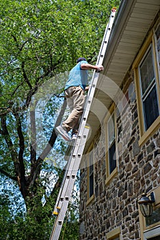Vertical side view of a man on a ladder cleaning gutters of a stone home