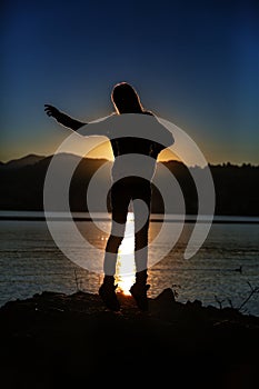 Vertical silhouette shot of a female jumping near the sea with the beautiful sunset in background