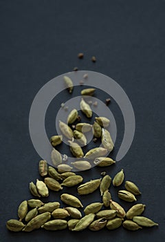 Vertical small DOF close up photo of Cardamom pods and seeds pile on the matt black background. It is very popular in Indian and