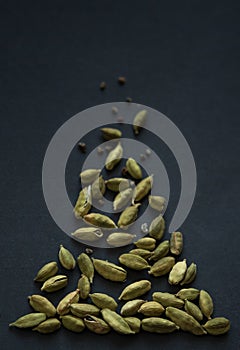 Vertical small DOF close up photo of Cardamom pods and seeds pile on the matt black background. It is very popular in Indian and