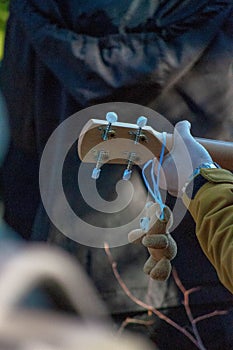 Vertical of a small teddy bear hanging from a headstock of a guitar in a man's hand