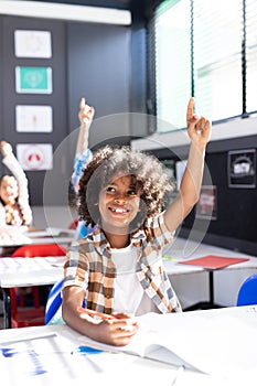 Vertical of smiling african american boy raising hand in elementary school classroom, copy space