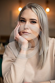 Vertical smiling beautiful attractive blond woman with make up, looking at camera, leaning on hand. First date. Close up