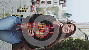 Vertical: Smiling young woman with coffee cup walking and talking on phone