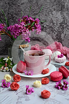 Vertical spring composition. A cup of tea, appetizing macarons, pink flowers and chocolate in the form of roses on a