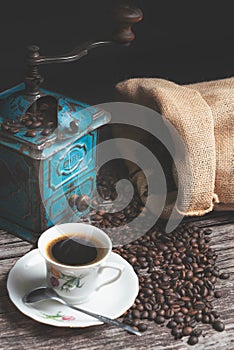 Vertical studio shot of still life with vintage manual green metal coffee grinder, jute bag and coffee beans on old