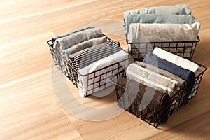 Vertical tidying up storage. Neatly folded clothes neutral colors in the metal black baskets for wardrobe. Wooden background.