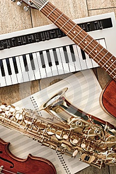 Vertical top view of different musical instruments: synthesizer, guitar, saxophone and violin lying on the sheets for