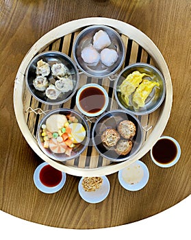 Vertical top view dim sum combination in chinese bamboo steamer on wooden table with a variety of dipping sauce