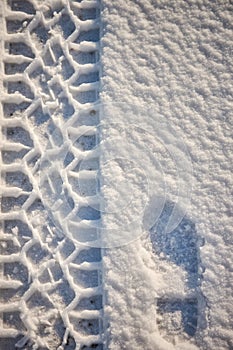 Vertical top view of a footprint and car wheel trail in the snow