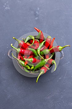 Vertical top view of the green and red hot chili peppers in a rusty cup on a dark tabletop