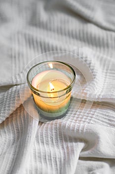 Vertical top view of a litten candle on a white comforter
