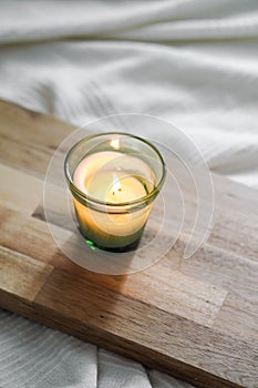 Vertical top view of a litten candle on a wooden board, on a white comforter