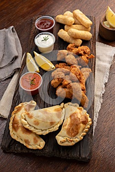 Vertical top view of a picada board with nuggets and tequenos with lemon slices and spicy sauces