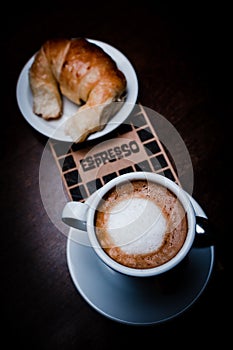 Vertical top view shot of a coffee and bread in a white cup and saucer on a smooth cafe table