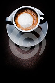 Vertical top view shot of a coffee latte in a white cup and saucer on a smooth cafe table