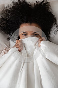 Vertical top view woman hides behind blanket looking at camera