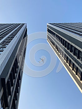 Vertical undershot of two skyscrapers with the airplane flying over the blue sky background
