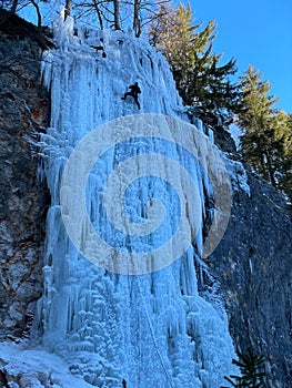 VERTICAL: Unrecognizable athletic man ice climbs up stunning frozen waterfall.