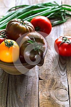 Vertical various tomatoes in clay bowl in contr light decorated with green fresh onion.