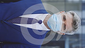 Vertical video. Close-up of the face of a handsome Caucasian businessman wearing a medical mask, looking directly into