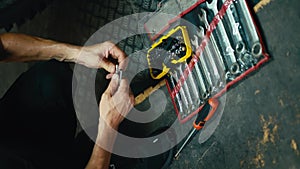 Vertical video: close-up: a male mechanic with his sinewy hands selects the tool he needs among a set of tools on the