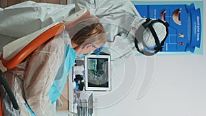 Vertical video Dentist in coverall examining x-ray image on tablet