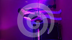 Vertical video of an energetic male rock band guitarist playing in neon light and smoke. Dancing guitar player in the