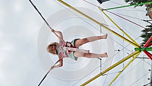 vertical video. little girl jumps on bungee trampoline. entertainment in park