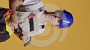 Vertical video: Portrait of silly contractor playing air guitar with hammer