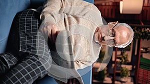 VERTICAL VIDEO POV Retiree man reading news and resting at home in evening, portrait of grandfather