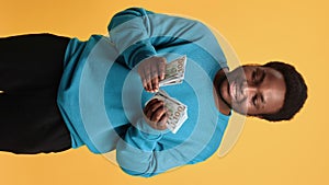 VERTICAL VIDEO POV young black man counting cash money and smiling, look at camera, medium portrait