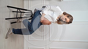 vertical video. pregnant woman in white shirt with bare tummy sits on chair