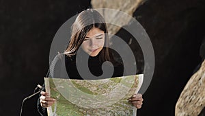 Vertical video. Travelling to the mountains. Hiker woman holds old map standing on the top of the rock. The tourist