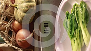 Vertical video of water droplets falling to a bowl of bokchoy soaking in the sink