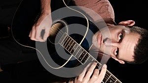 Vertical Video. Young Man Blogger Plays an Acoustic Guitar on a Black Background