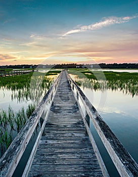 Vertical view of a beautiful sunset over coastal waters with a very long wooden boardwalk pier in the center during a colorful sum