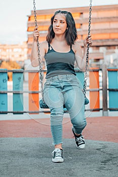 Vertical view of a beautiful young girl sitting on a swing while staring off into the distance